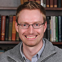 Derrick Wirtz, a man with short red hair and thin-rimmed glasses, smiling in front of a bookcase.