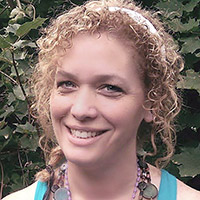 Karen E. M. Henry, a woman with curly strawberry-blonde hair and a white headband, smiling in front of an ivy-covered wall.